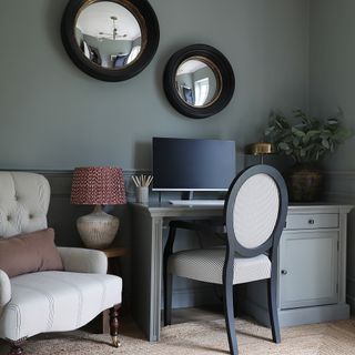 a study desk area with an armchair, desktop computer and a pair of black and gold framed convex mirrors on the wall