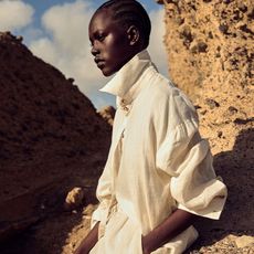 model wears white linen separates while leaning against rock 