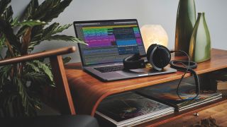 A MacBook on top of a table with a DAW on its screen and studio headphones