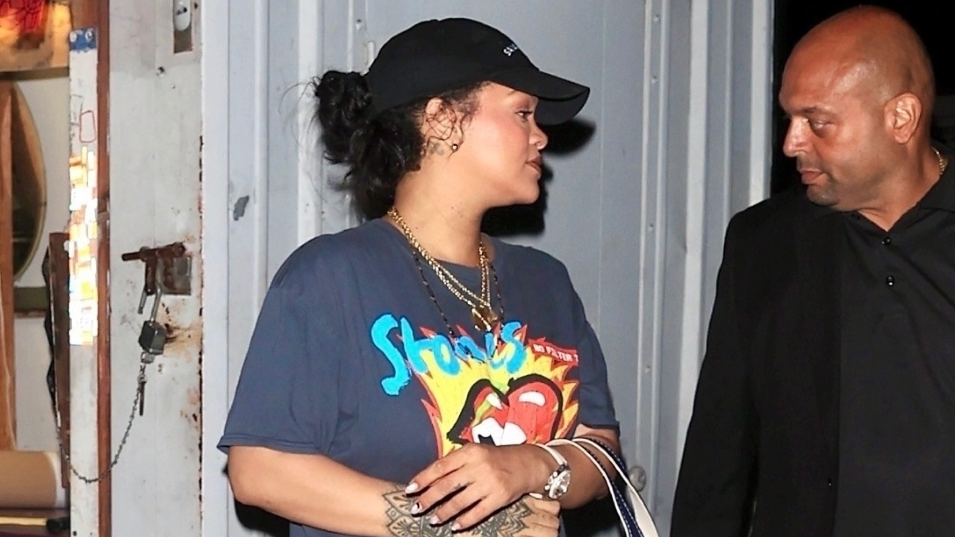 Rihanna wears a graphic T-shirt and sneakers and carries a tote bag