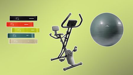 Aldi exercise bike surrounded by five vertically stacked resistance bands and a gray exercise ball on a green background fading from right to left