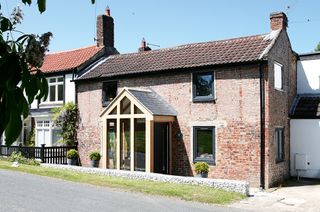 a small house extension of a large porch and lobby on a large brick home, with a small brick wall; by Gemma Medden and Gareth Fisher's extended cottage in Hornby, North Yorkshire