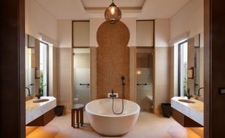Bathroom in the Banyan Tree Tamouda Bay hotel with large stone bathtub, wiled walls and glass doors leading to a shower