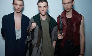 3 male models in dark clothing, holding handbags