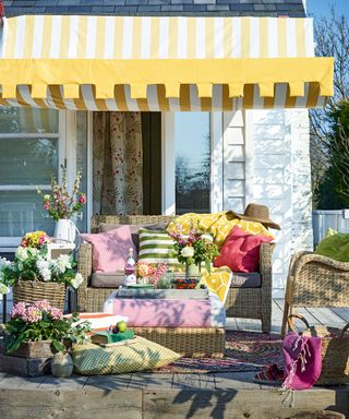 An example of garden shade ideas showing a yellow and white awning over rattan garden furniture with colorful cushions