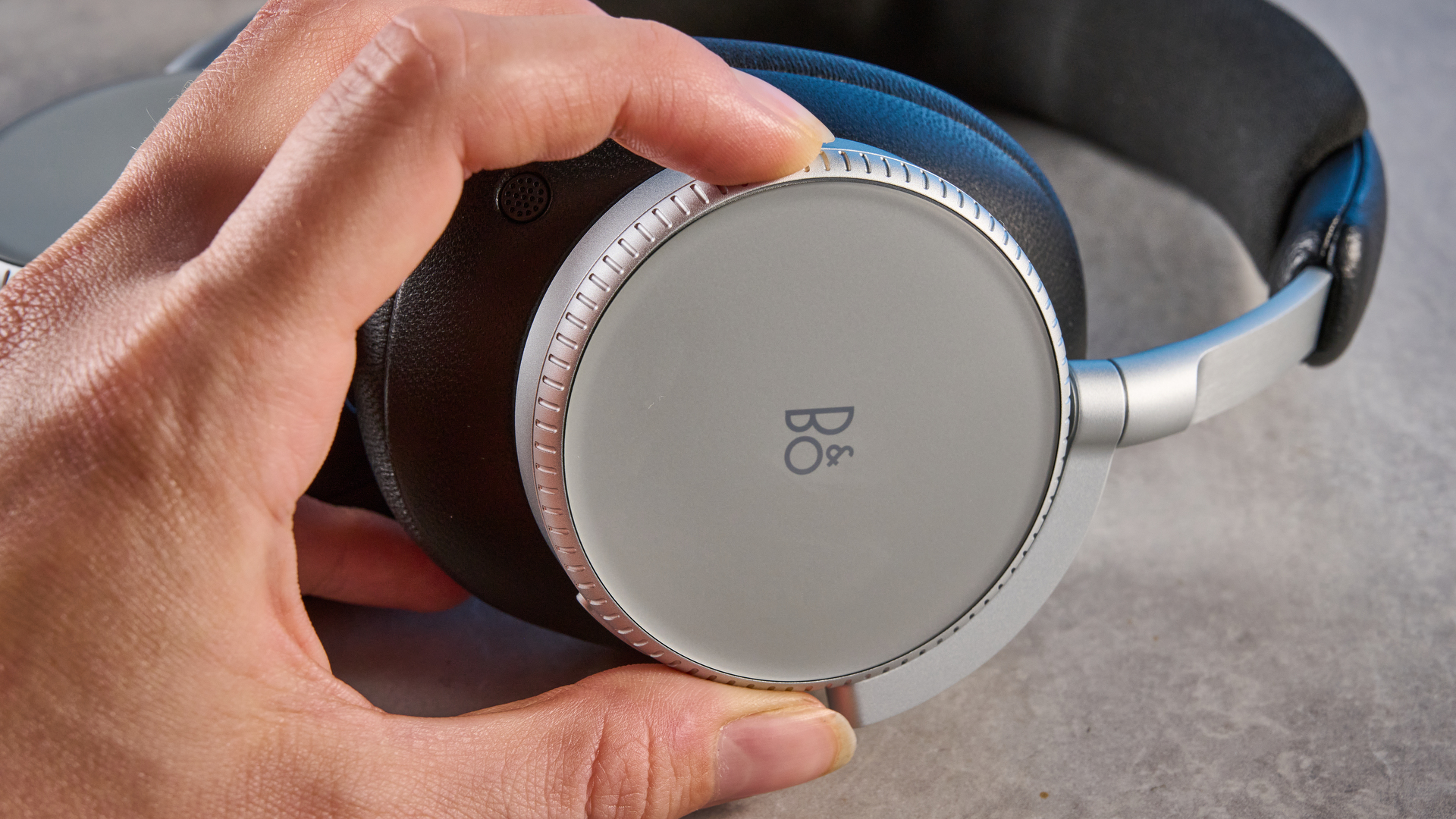 The Bang &amp;amp; Olufsen Beoplay H100 earcups in hand on a stone surface
