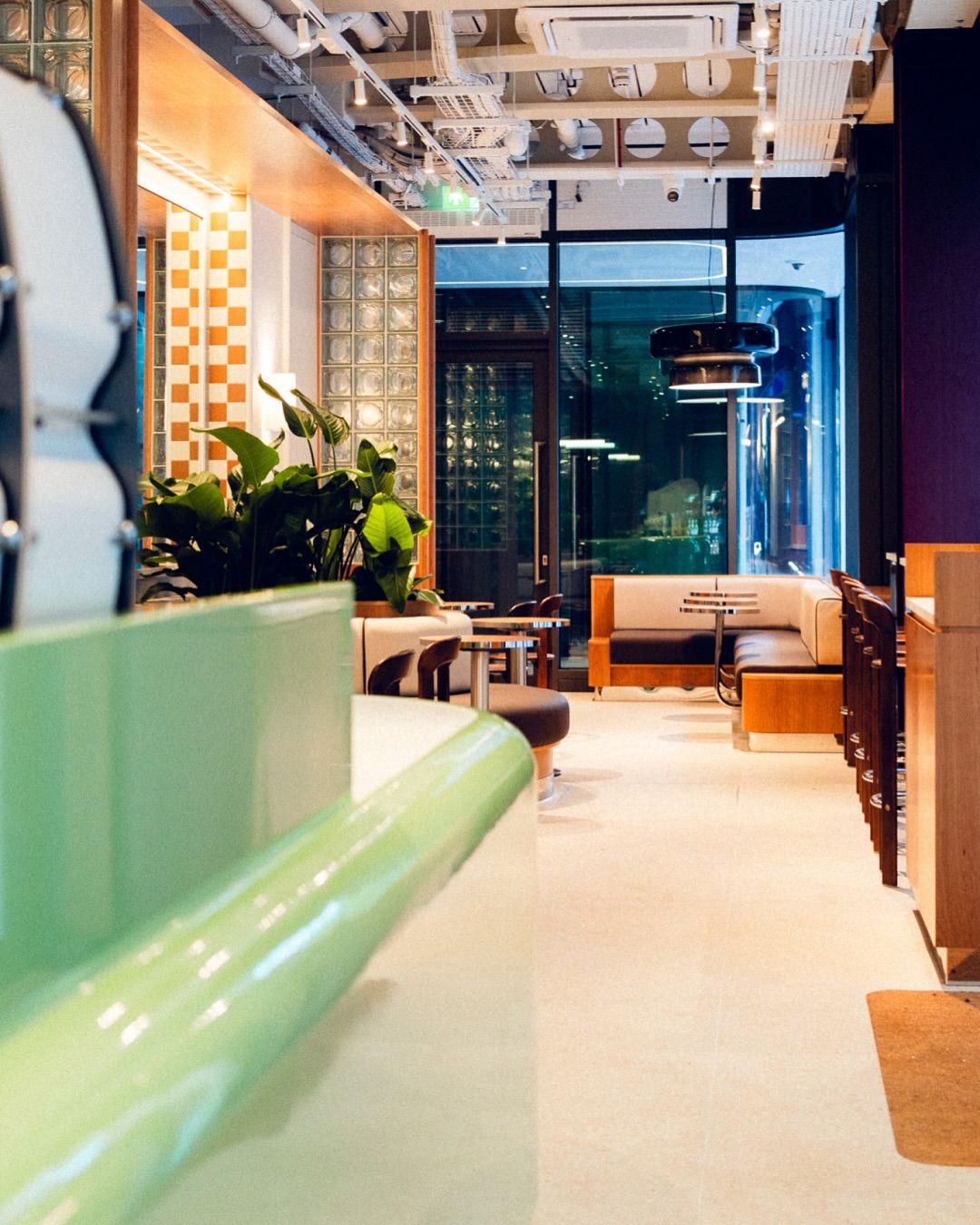 A Space Age-inspired matcha cafe with vivid furnishings, lacquered green bar counters, glass block walls, and wooden decor.