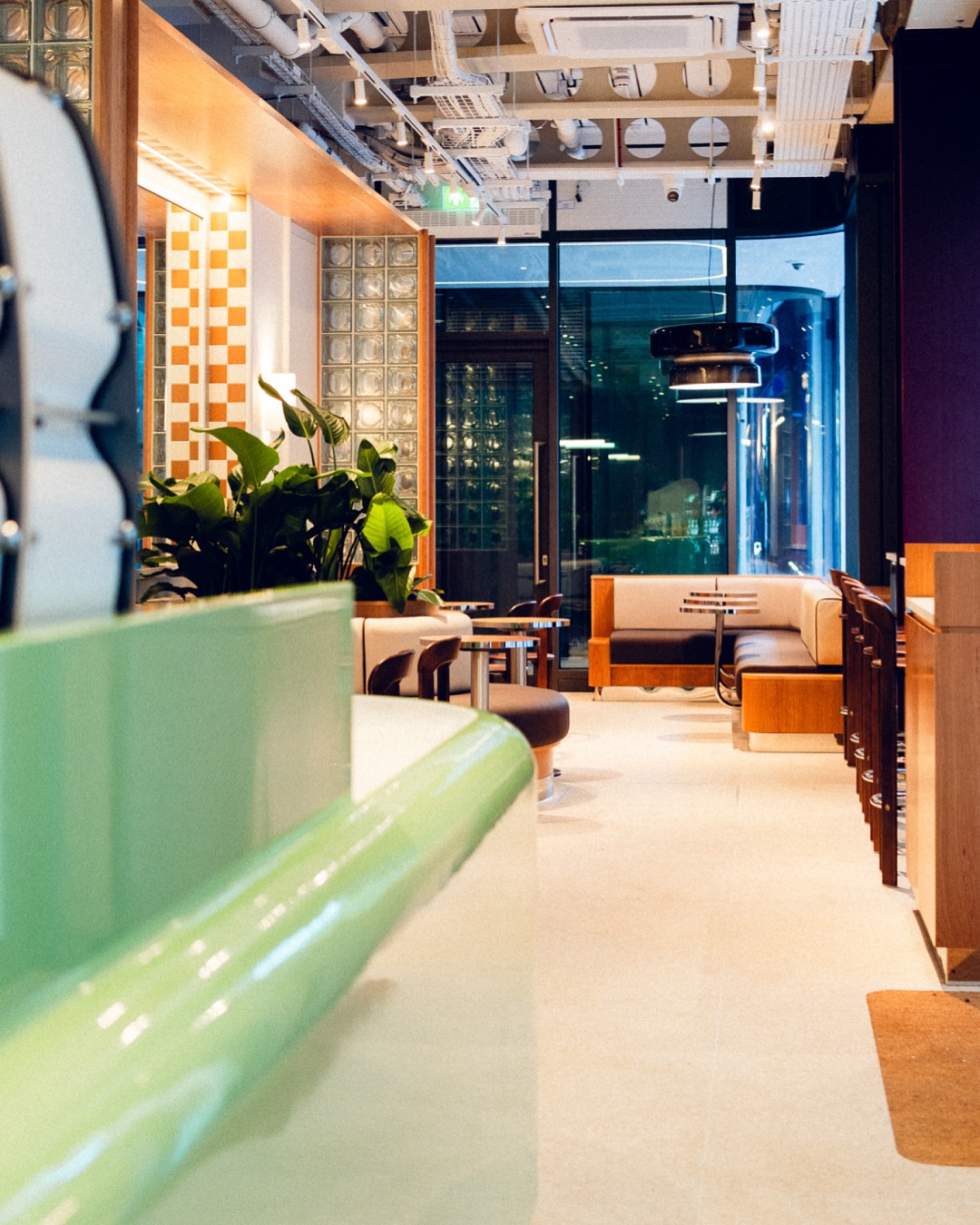 A Space Age-inspired matcha cafe with vivid furnishings, lacquered green bar counters, glass block walls, and wooden decor.