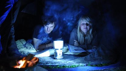 best camping lantern: two people in a tent reading using a camping lantern