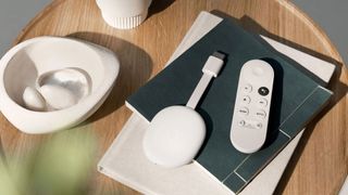 Chromecast with Google TV on a pile of books next to a plant pot