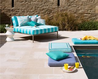 An example of pool party ideas showing a patio area next to a pool with a blue and white striped double sun lounger and cushions