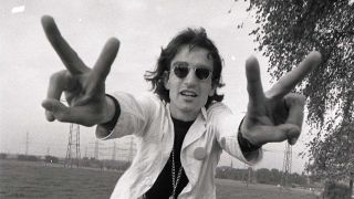 David Peel standing in a field making peace signs with his hands