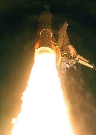 Flaming exhaust spews from beneath one of the two solid rocket boosters on space shuttle Columbia, as it roared into the night sky on the STS-93 mission, which launched on July 23, 1999.