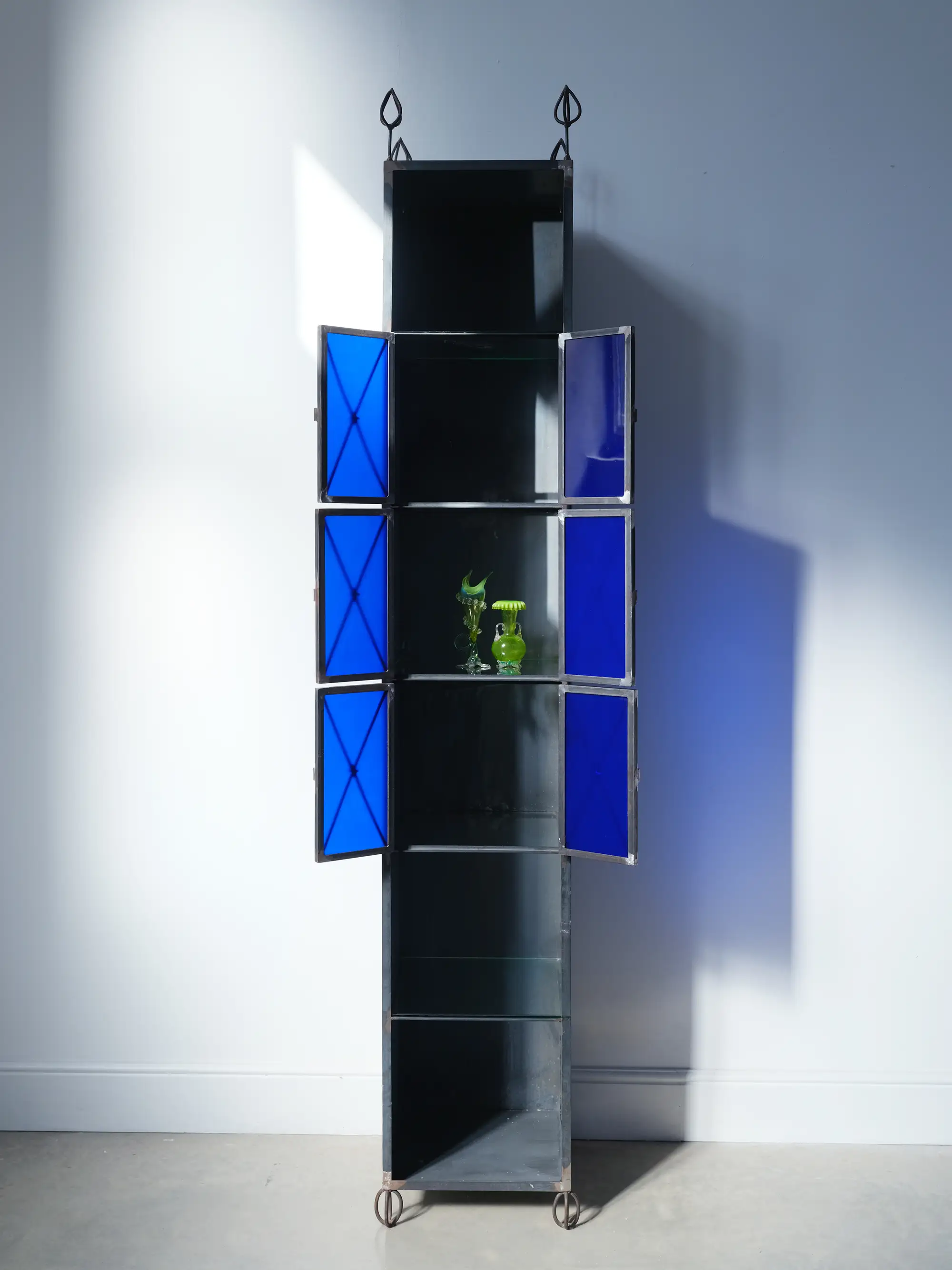A boxy metal cabinet with six shelves, three of which have cobalt blue glass doors covering them.