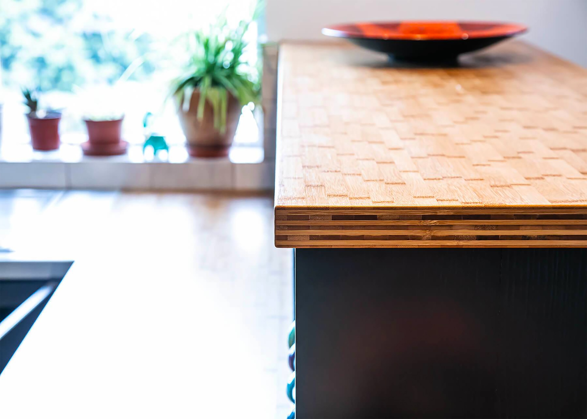 A bamboo kitchen worktop with a bowl on top of it as well as a view of potted plants by a kitchen windowsill