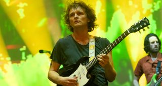 Stu Mackenzie of King Gizzard and the Lizard Wizard plays a Gibson SG on a stage illuminated by green and yellow lights 