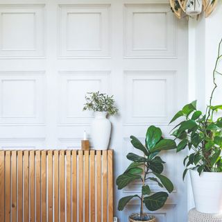 A living room with light grey-painted Jacobean-style wall panelling and a radiator cover made with vertical wooden slats