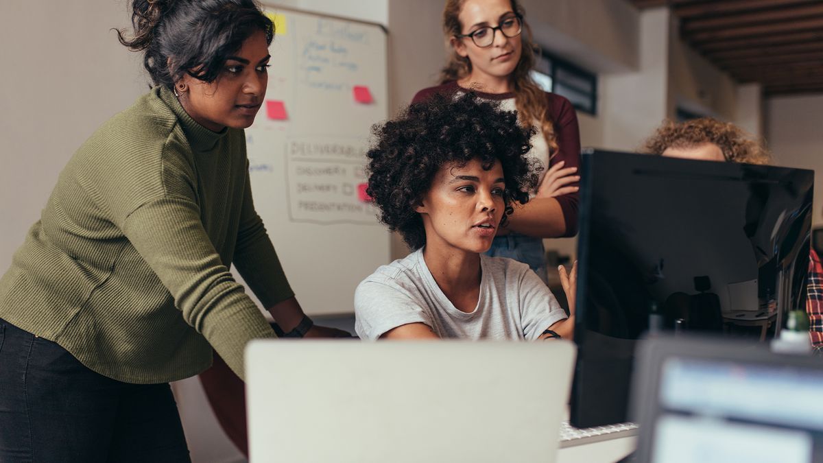 Team of all-female startup founders discussing project around a computing station in an office space.