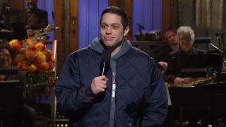 Pete Davidson holding up a mic with his left hand during his Monologue on SNL.