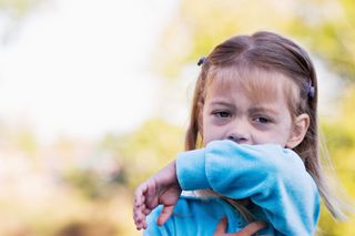 A little girl breaths into the crook of her arm.