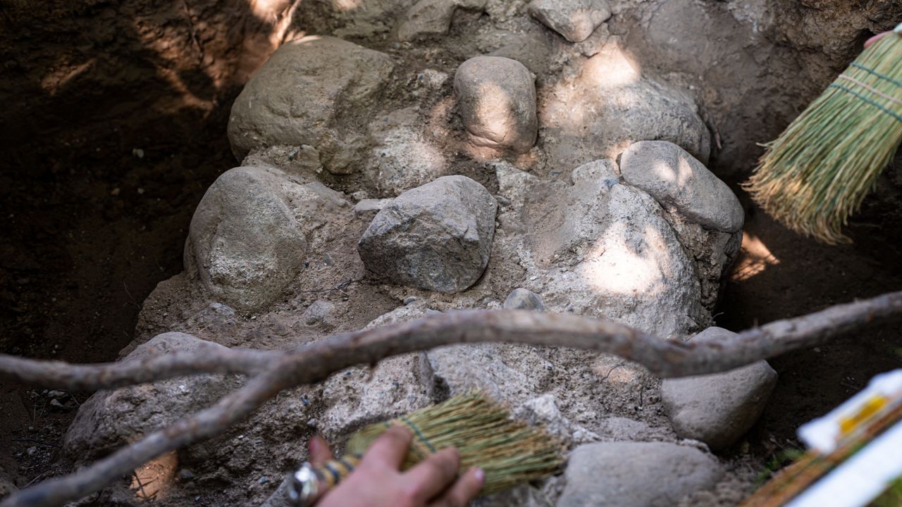Stones and cement surrounded by dirt. They are being brushed off with brooms.