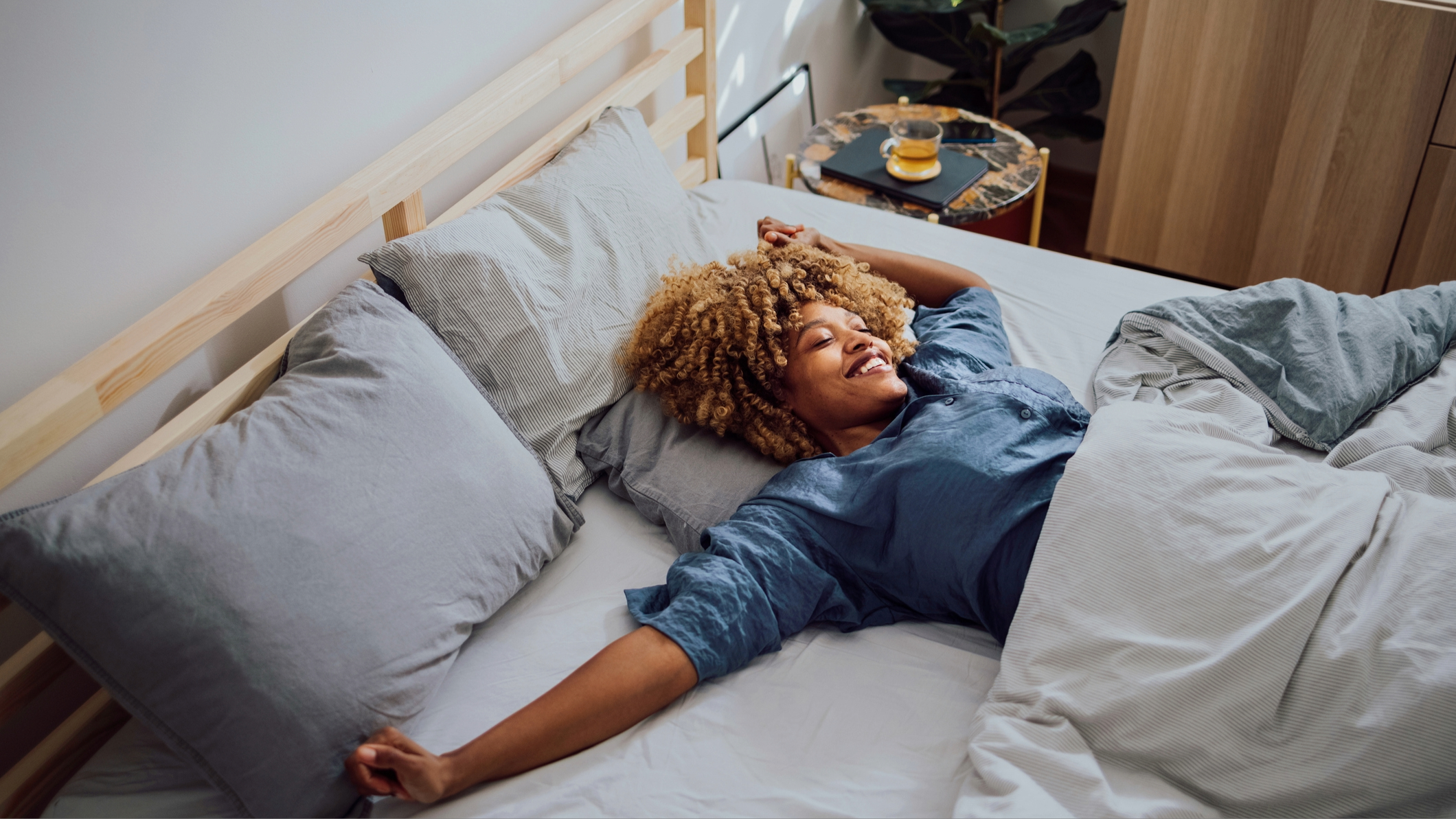 A woman lying on her back in bed stretching as she wakes up smiling