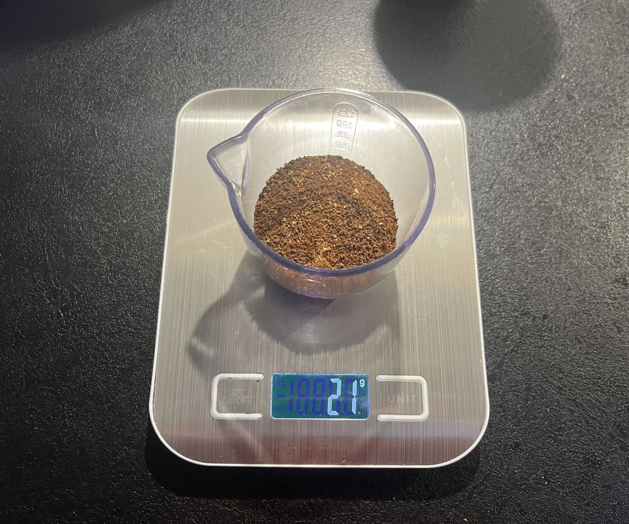 medium ground coffee beans in a clear plastic container on digital weight scales.