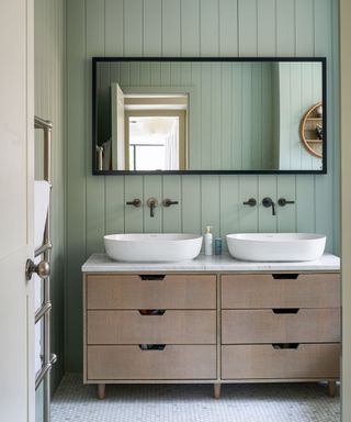 A modern bathroom with a green paneled wall and a twin basin