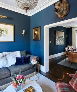 A small living room with blue walls and wood floor leading through to a dining room with navy blue walls.