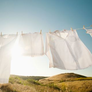 white clothes drying on a washing line outside with the sun shining behind
