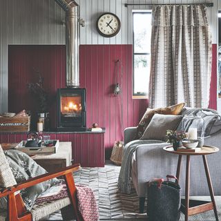 A living room with wall panelling and a colour-blocked wall in grey and burgundy with a wood burning stove