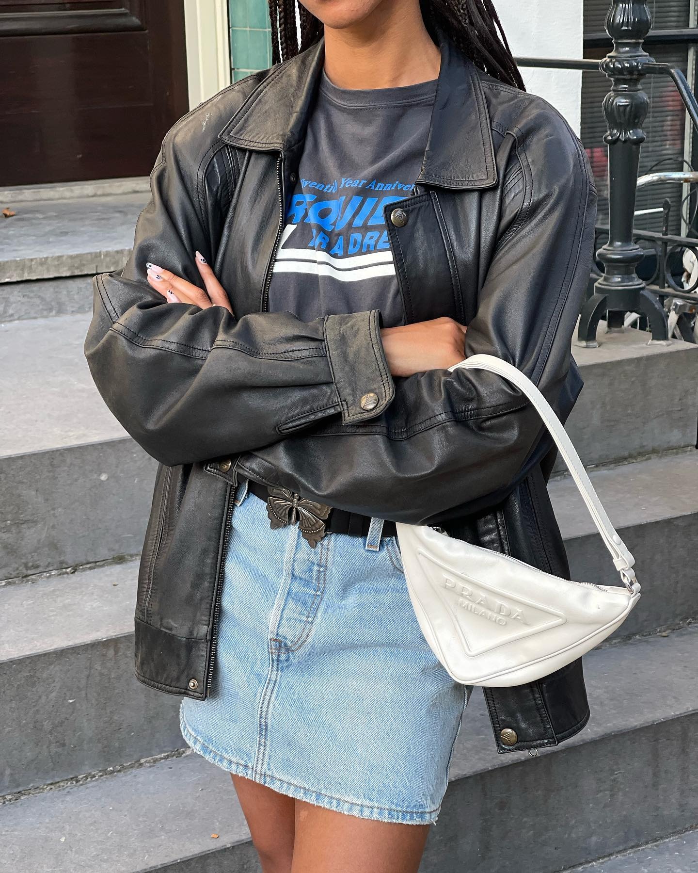 Fashion person Amaka wears a black leather bicker jacket a slogan t-shirts and denim mini skirt and carries a white Prada logo bag in an image taken from her Instagram recently.