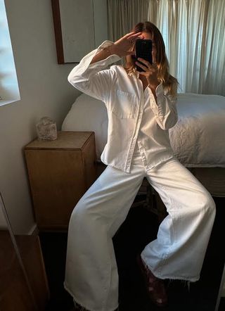 Woman takes photo in mirror wearing white denim top and trousers