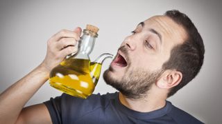 Man holding a jug of olive oil and pretending to drink from the spout