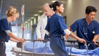 Doctor and nurses wheeling patient in gurney through hospital corridor.