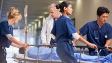 Doctor and nurses wheeling patient in gurney through hospital corridor.