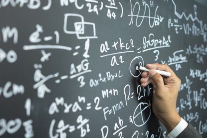 A hand writes formulas on a chalkboard.