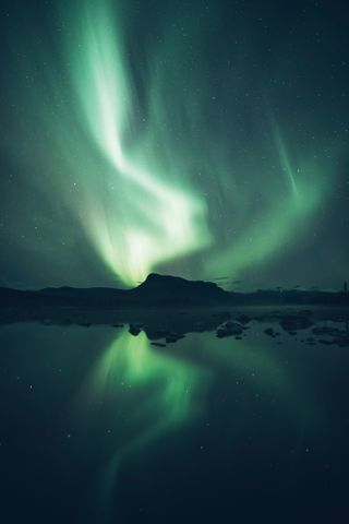 Northern lights over a rock formation and lake in Sweeden, tones of green and black, by Eeva Mäkinen