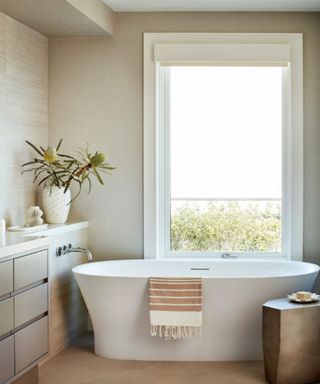 A bathtub in front of a window with a towel draped over the side