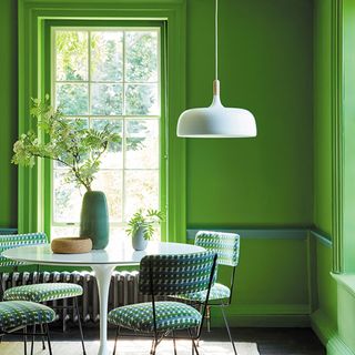 Bold green dining room with white pedestal dining table and pendant light