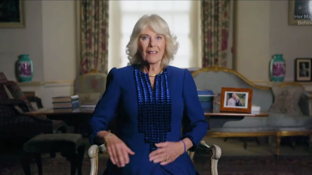 Queen Camilla wearing a blue dress sitting on a chair during Her Majesty the Queen: Behind Closed Doors