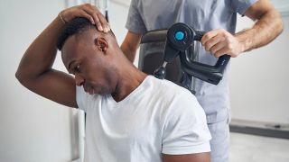Massage therapist using massage gun on man’s neck