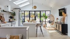 Kitchen-diner with soft off-white units and island, black metal wire bar stools, Crittall-style doors, herringbone wood floor, black and cane sideboard and natural textural details