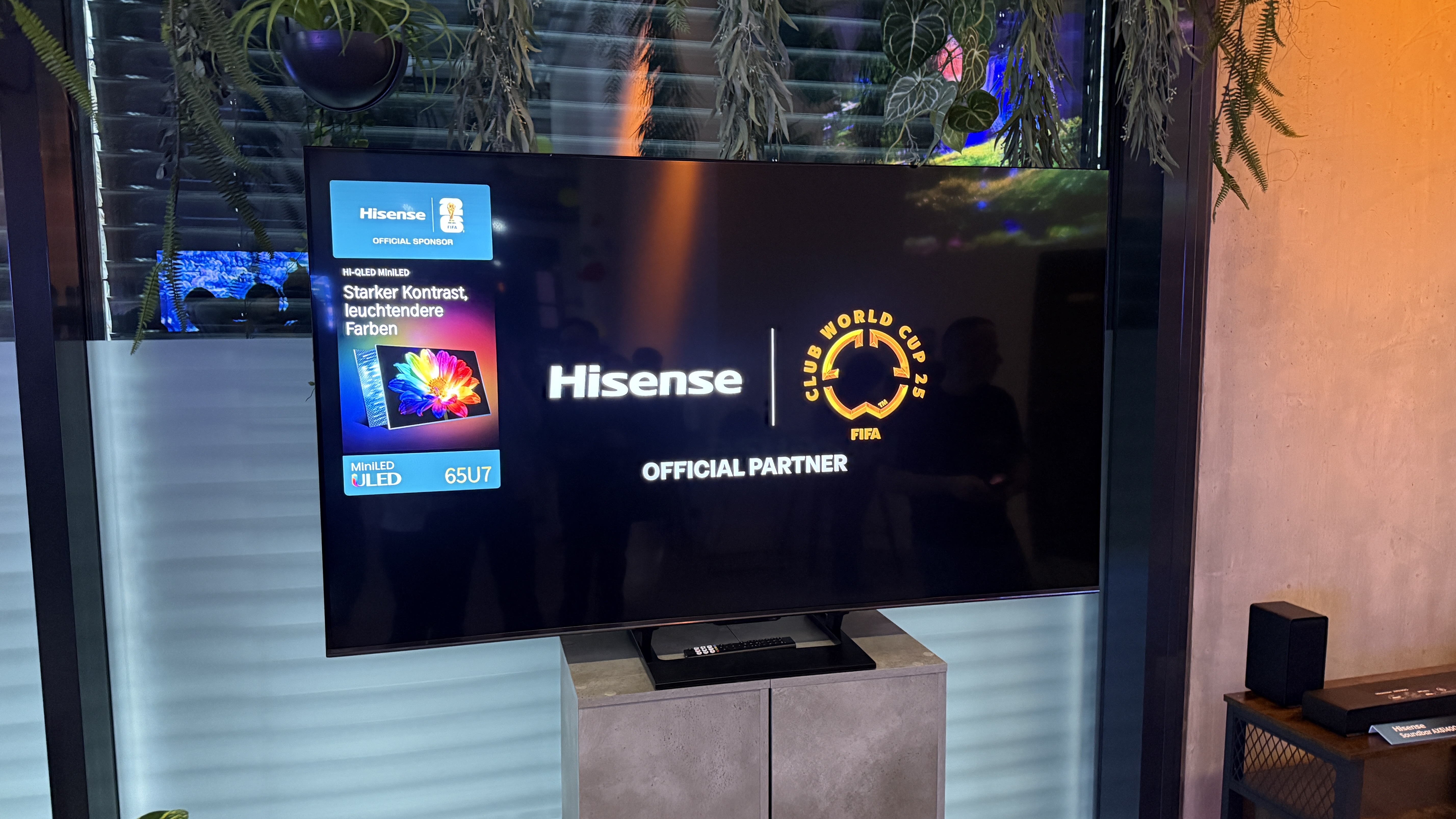 The Hisense U7S TV in an exhibition room, showing a black screen with the Hisense logo, with reflections visible on the black screen