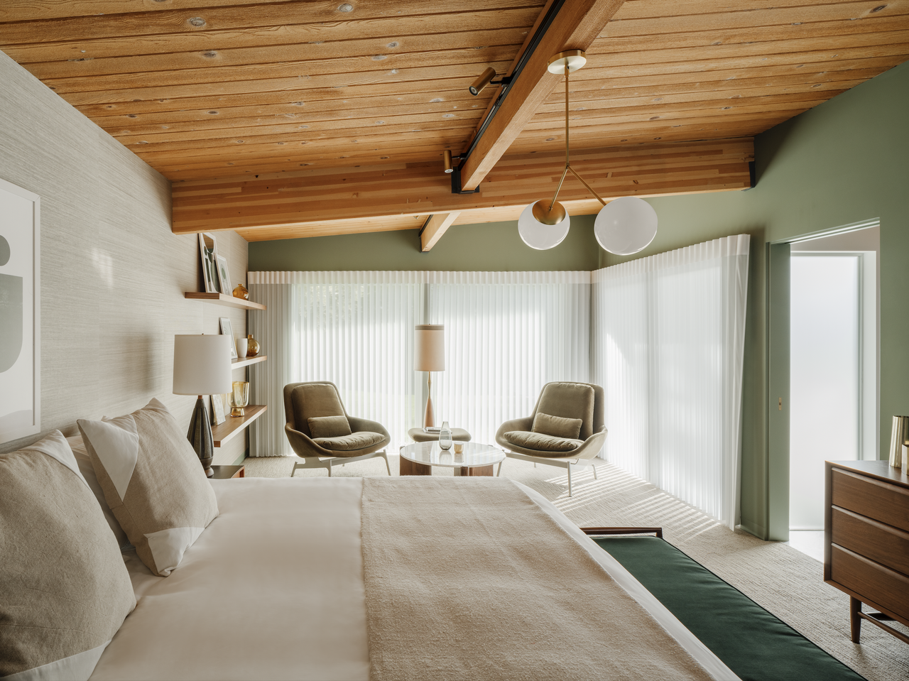 A bedroom with sage green walls, wooden beams, a cream bedding 