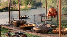 A vintage-style cast iron pan collection on an outdoor table, in front of a river. 