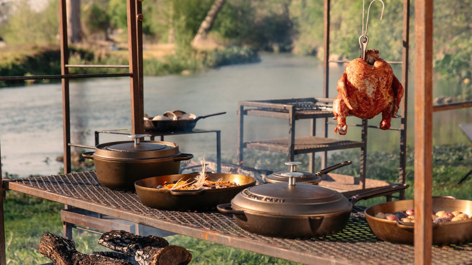 A vintage-style cast iron pan collection on an outdoor table, in front of a river. 