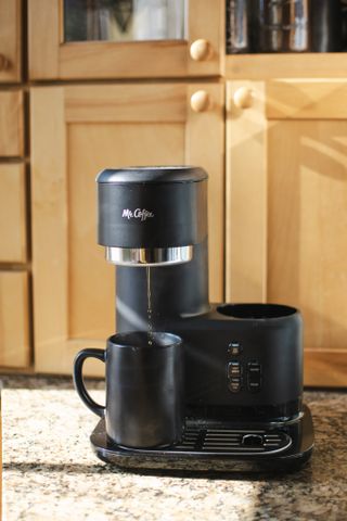 Making a black coffee in a matt black ceramic mug using the Mr. Coffee® Single-Serve Frappe™, Iced, and Hot Coffee Maker and Blender on a granite-effect kitchen worktop (Front-on perspective)