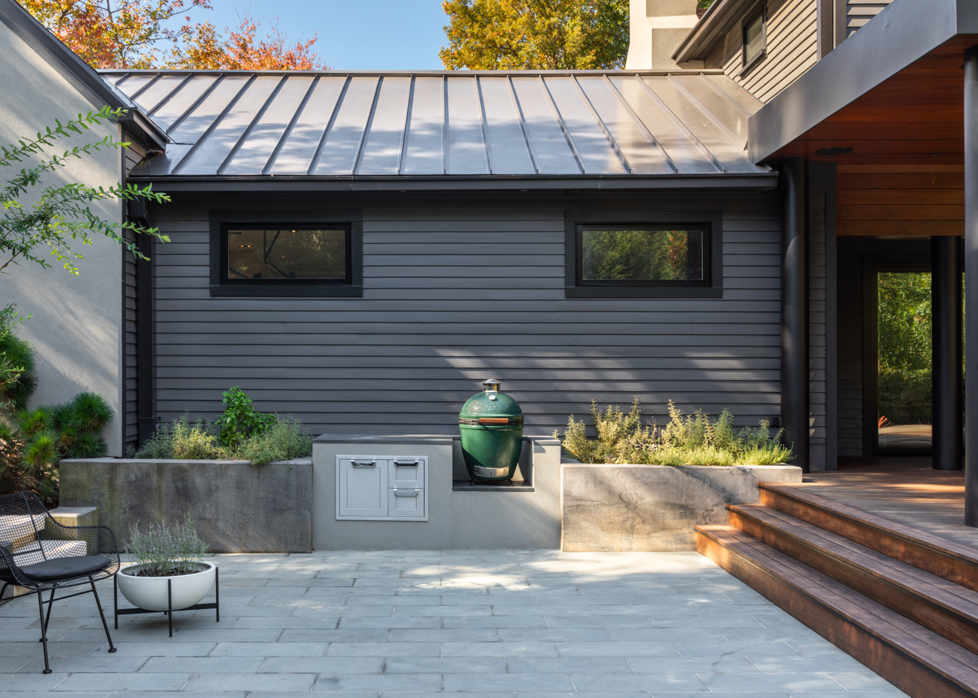 a backyard with a grey patio and timber decking and a big green egg grill in the middle of the patio.