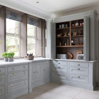 Grey kitchen cabinets with a built-in pantry, white floors, and windows overlooking the garden
